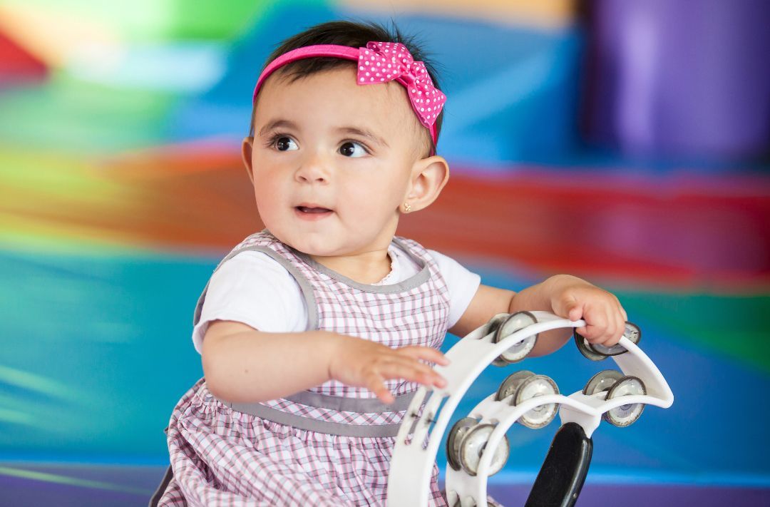 A baby girl is playing with a tambourine