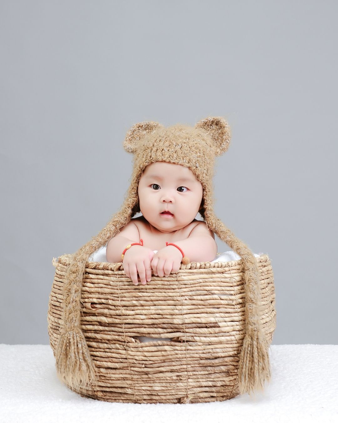 A baby wearing a teddy bear hat is sitting in a wicker basket