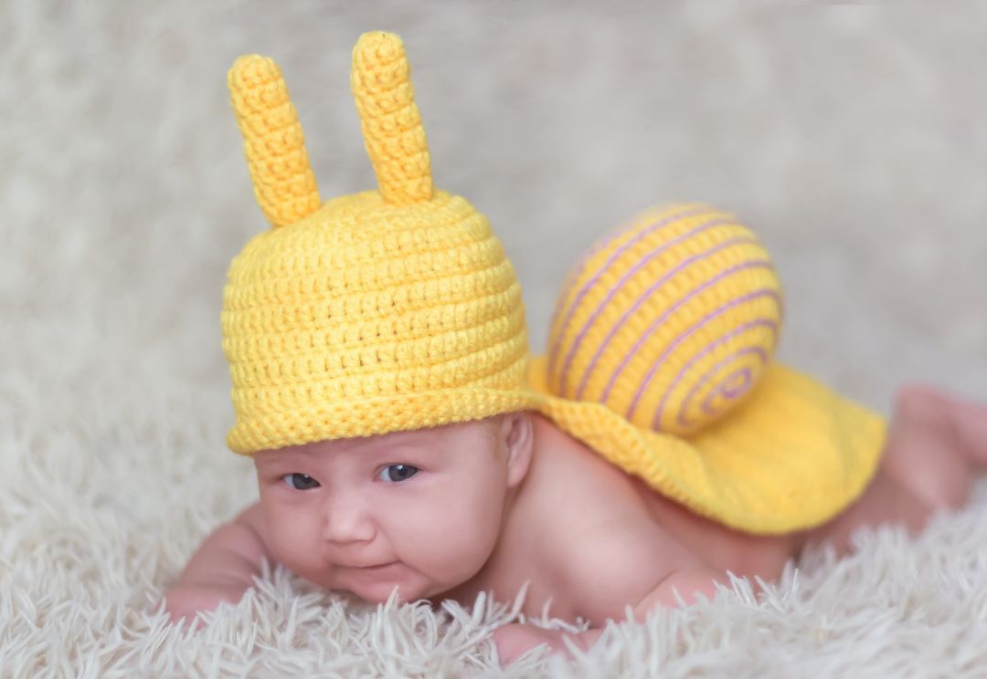 A baby wearing a yellow snail costume is laying on a carpet
