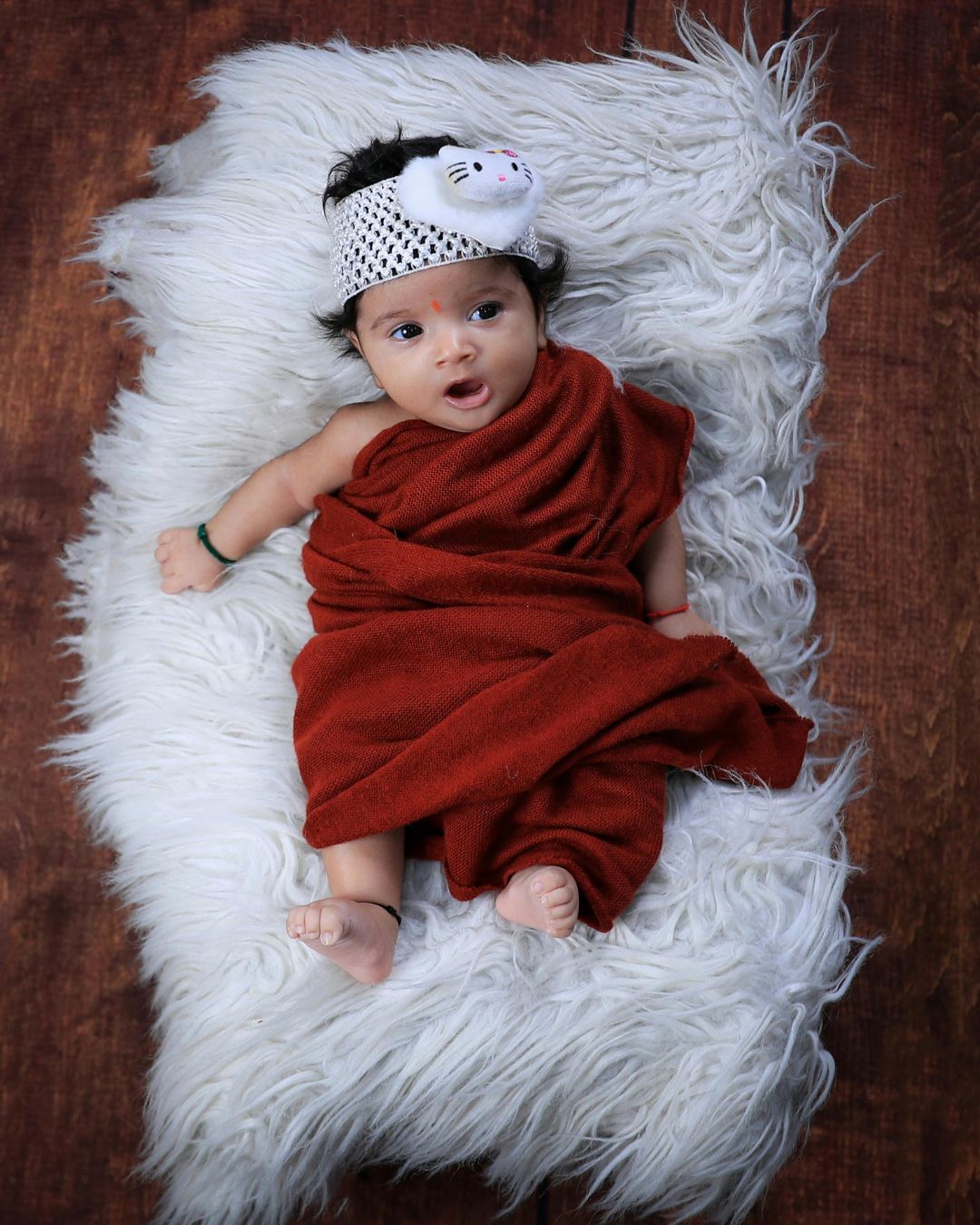 A baby wrapped in a red blanket is laying on a white blanket