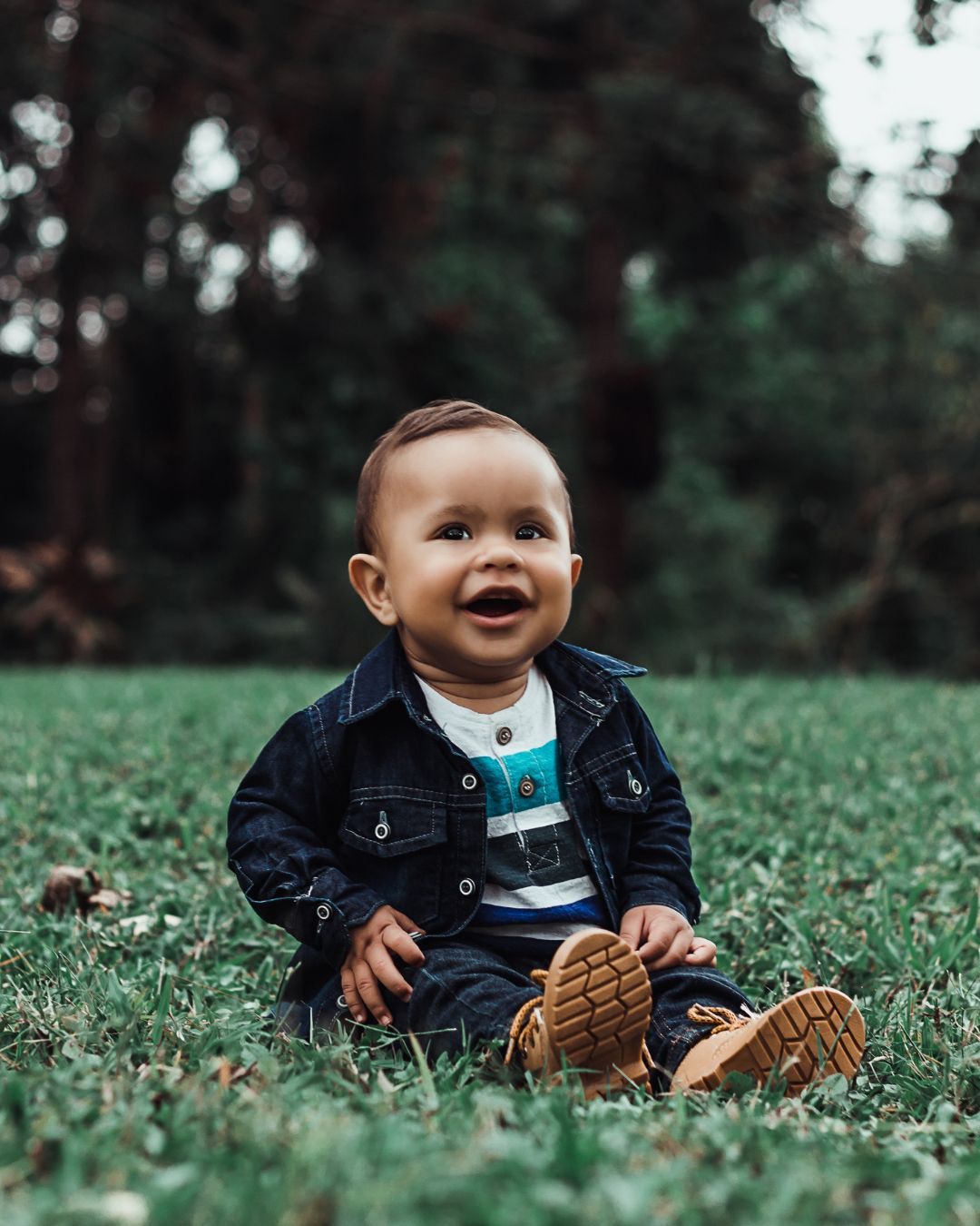 A baby is sitting in the grass and smiling