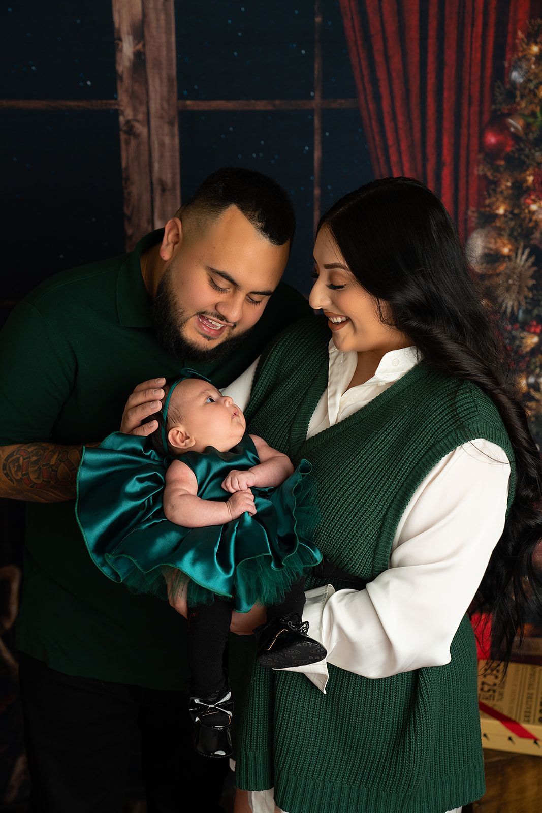 Parents holding a baby in front of a Christmas tree