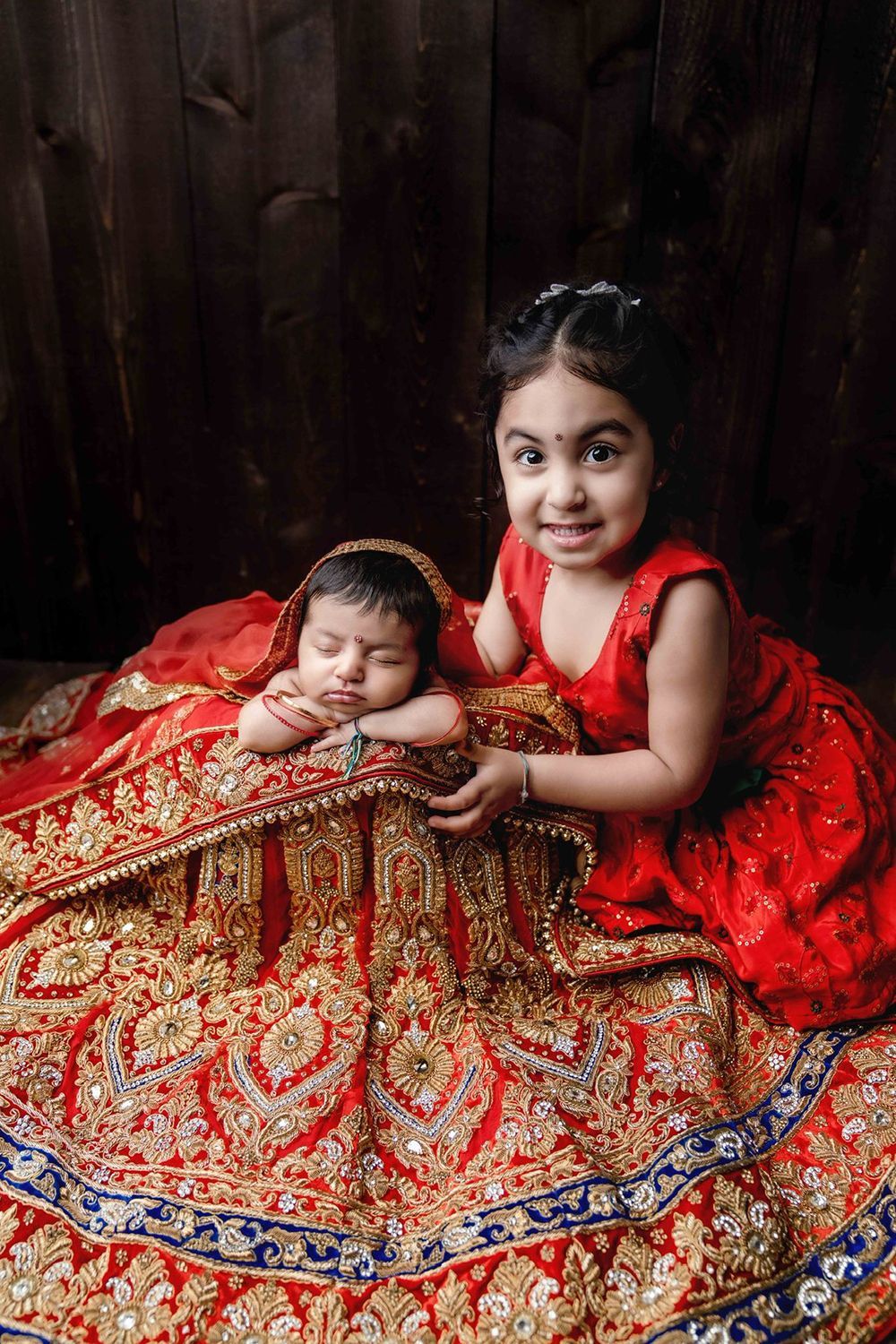 A little girl in a red dress is holding a baby in a red and gold dress