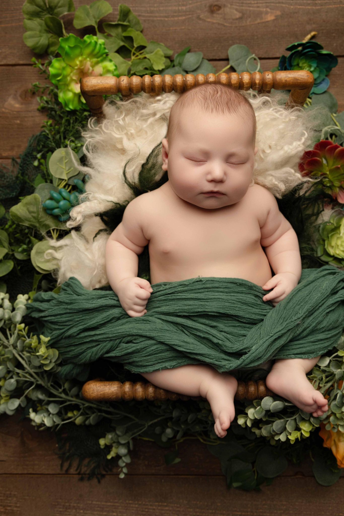 A newborn baby wrapped in a green blanket is sleeping in a wooden crib.