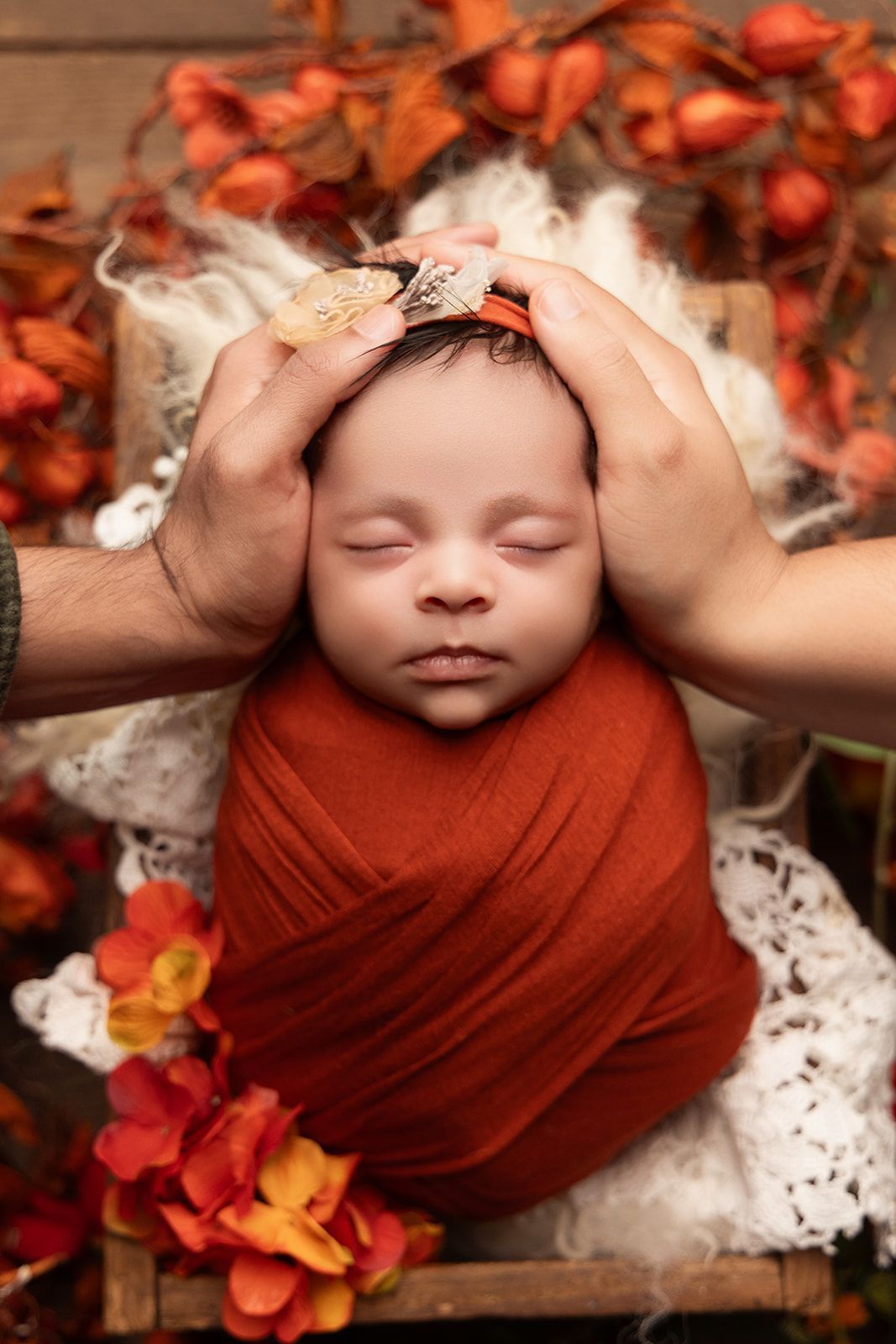 A newborn baby wrapped in a red blanket is being held by two people.
