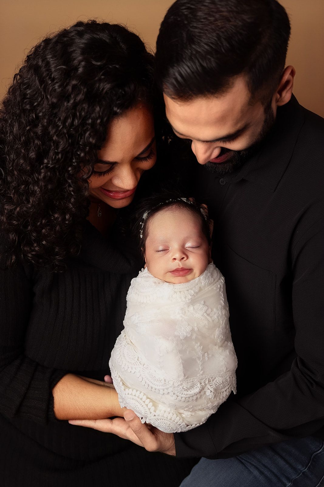 A man and woman are holding a newborn baby wrapped in a white blanket.