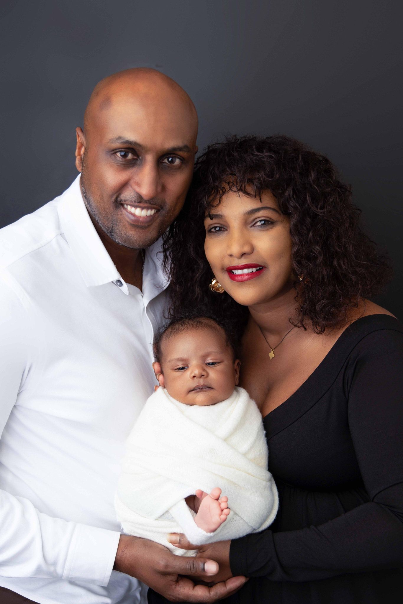 A man and woman are posing for a picture with their newborn baby.