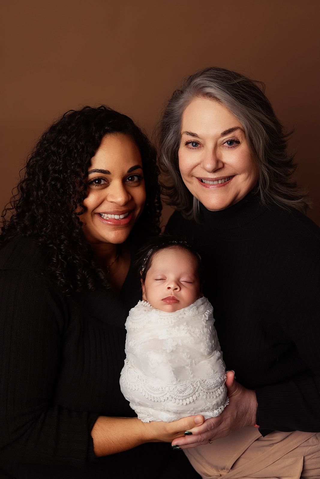 Two women are holding a newborn baby wrapped in a white blanket.