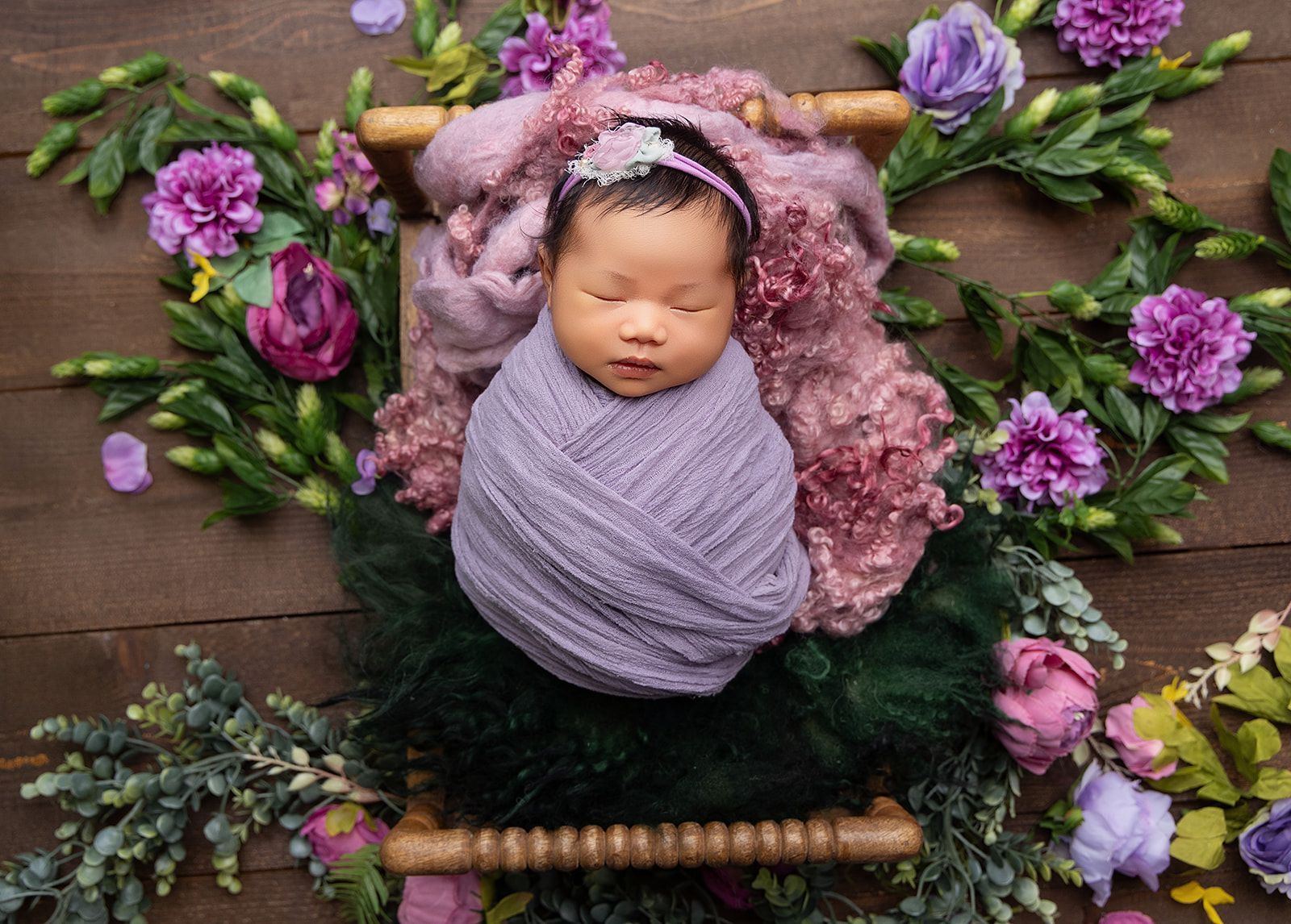 A newborn baby is wrapped in a purple blanket and surrounded by purple flowers.