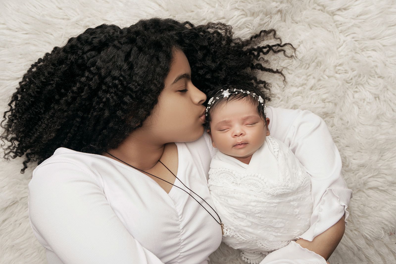 A woman is holding a newborn baby wrapped in a white blanket.