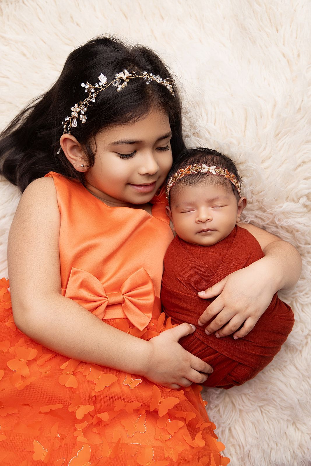 A little girl is holding a newborn baby wrapped in a red blanket.