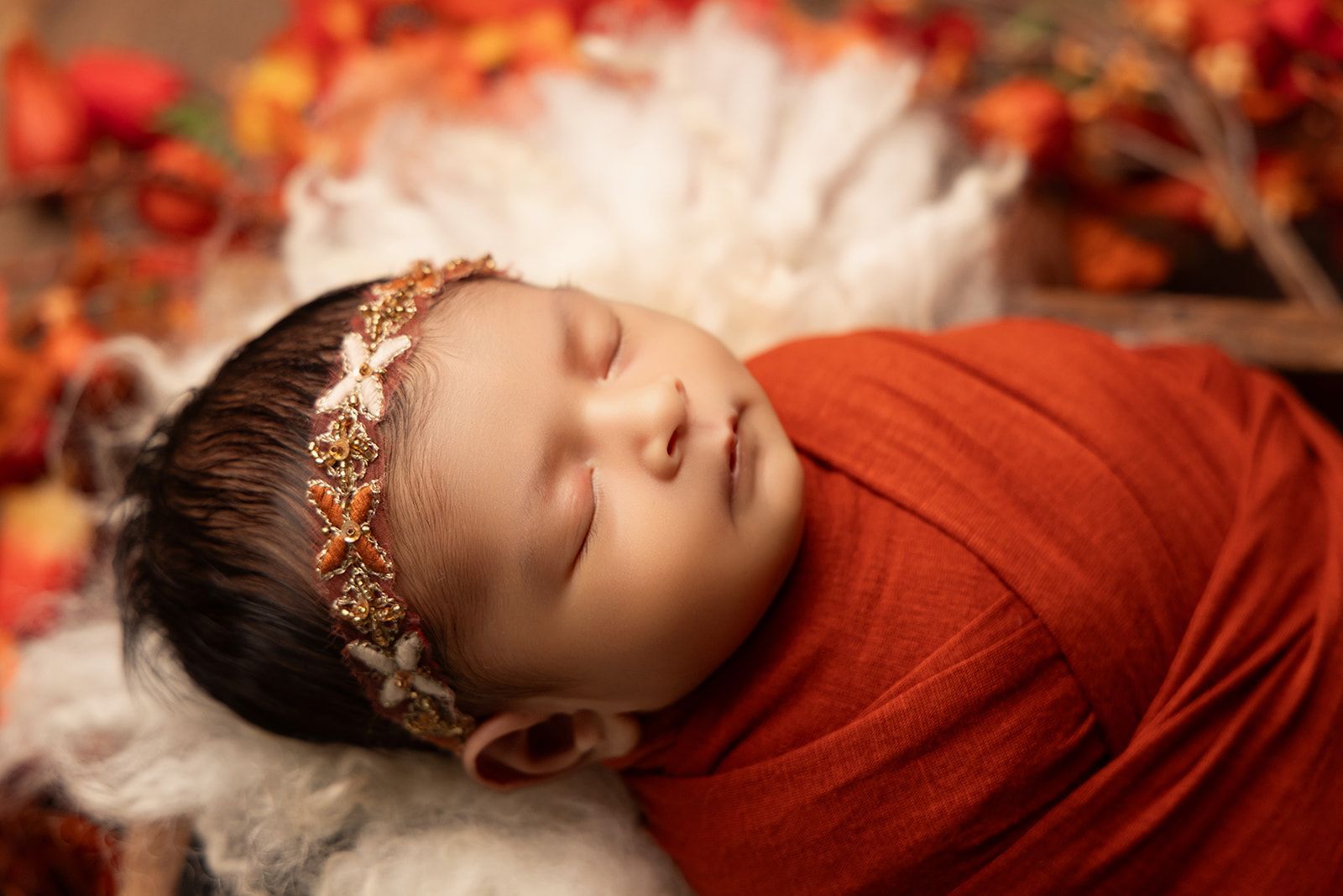 A newborn baby wrapped in a red blanket and a headband is sleeping.