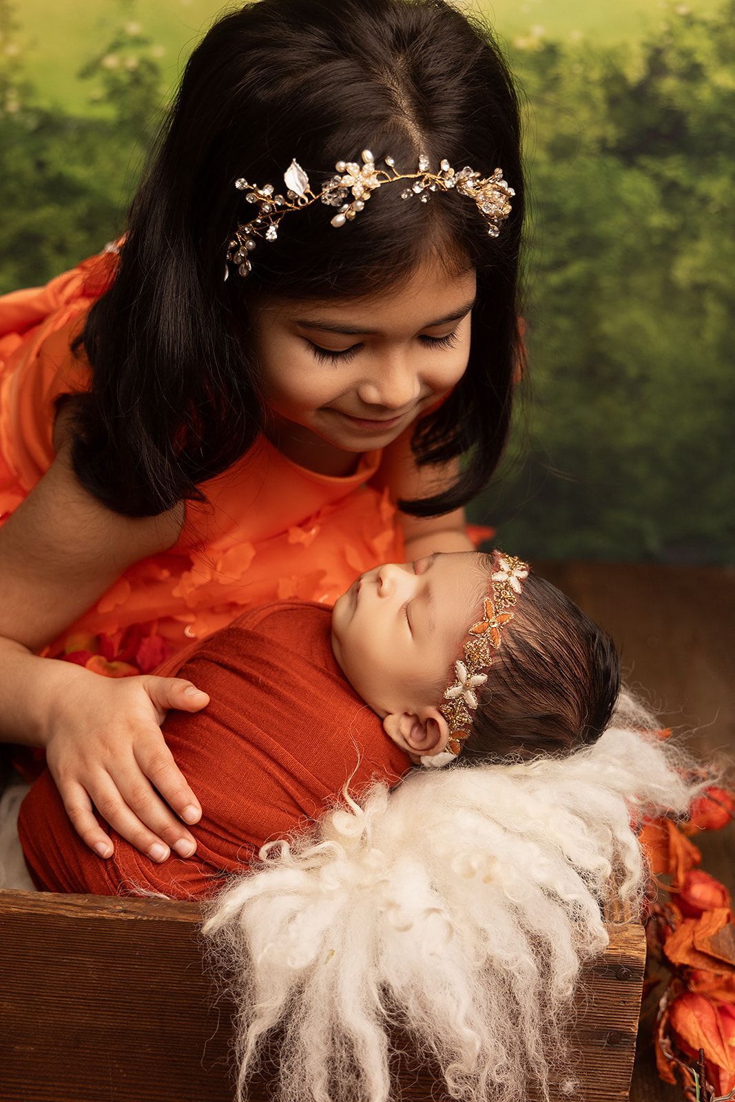 A little girl is holding a newborn baby in a basket.
