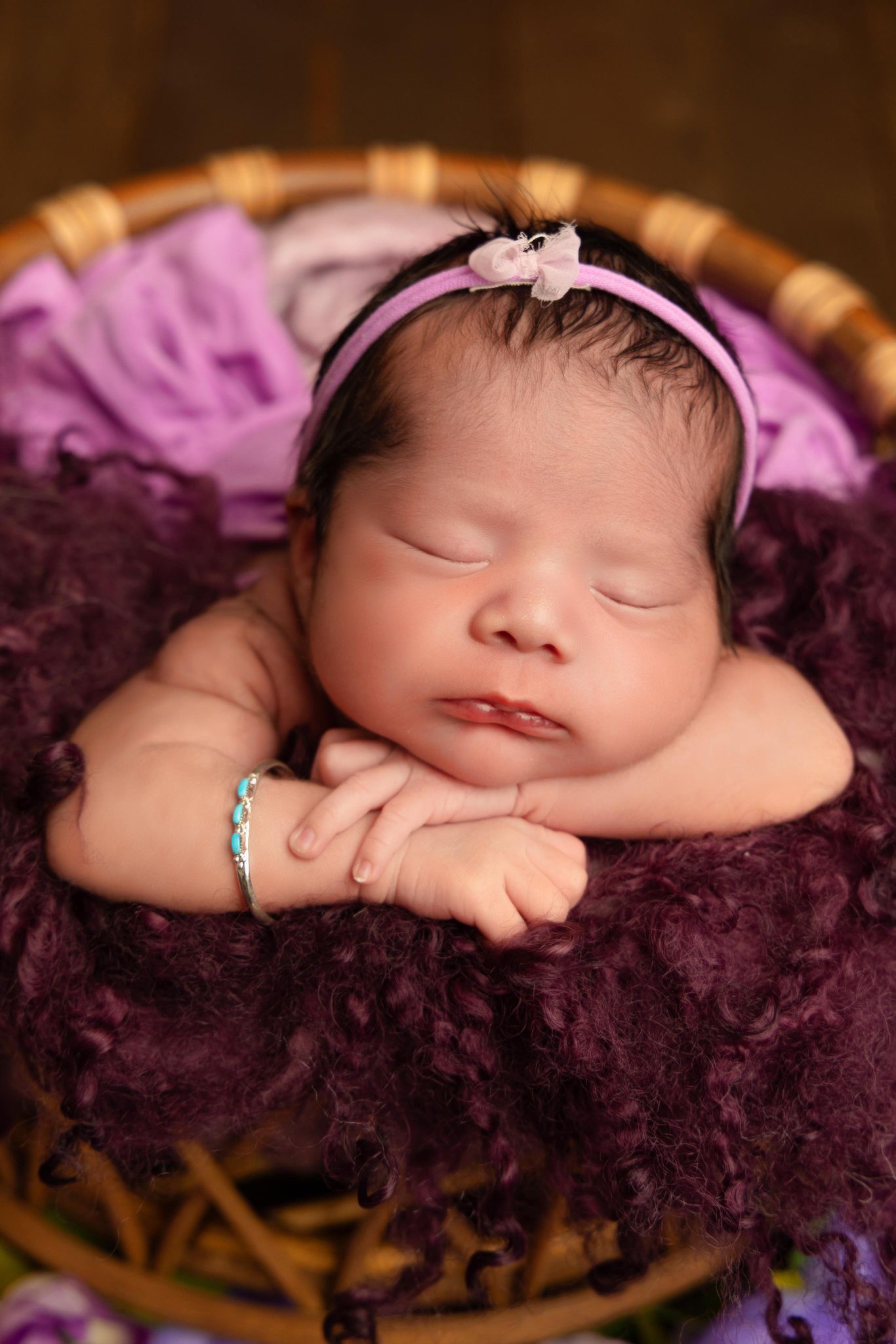 A newborn baby girl is sleeping in a purple basket.