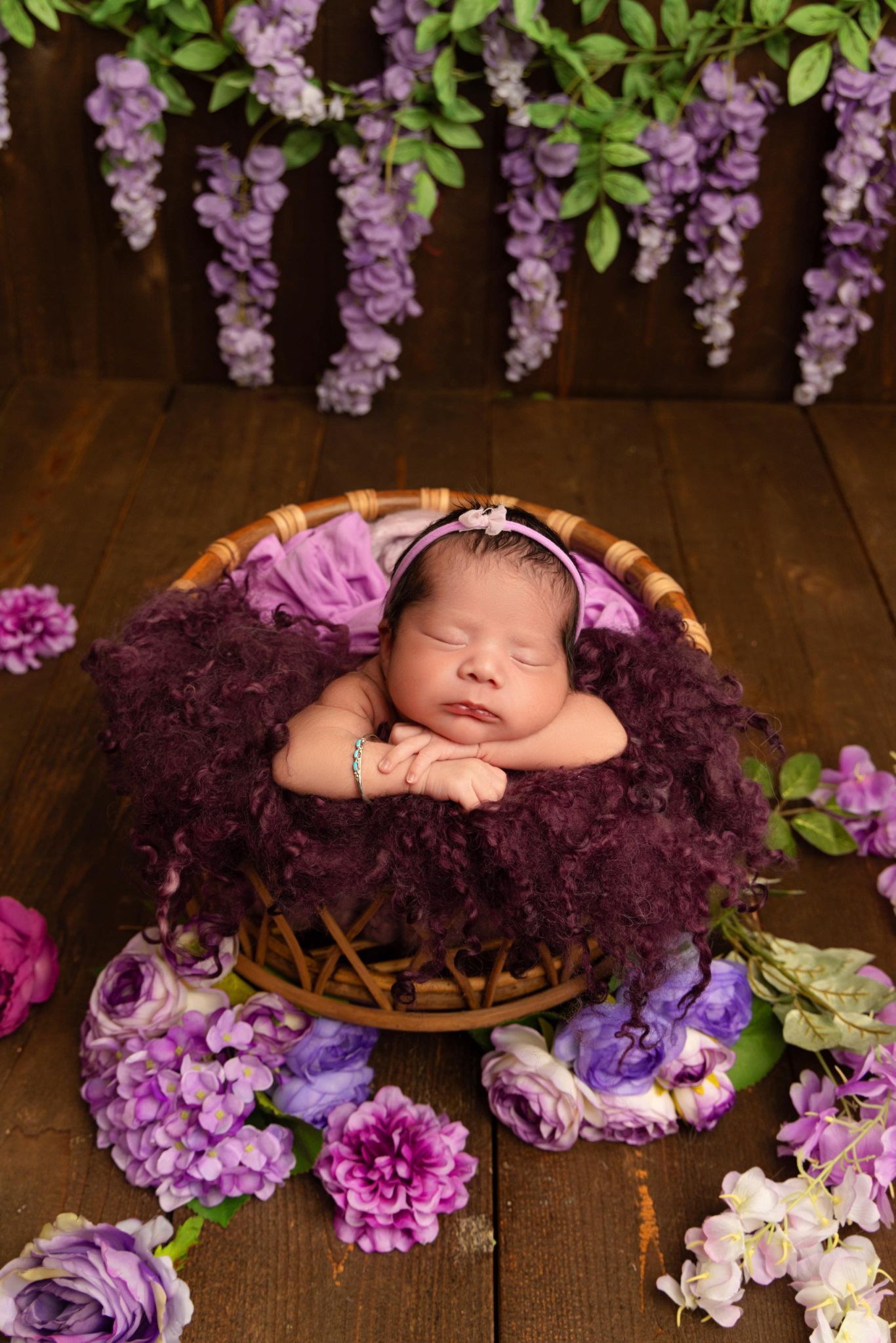 A newborn baby is sleeping in a basket surrounded by purple flowers.