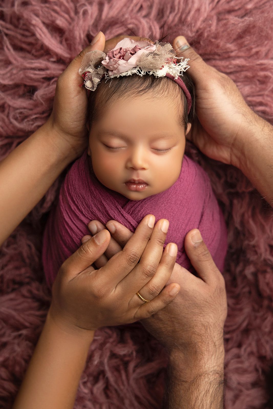 A newborn baby wrapped in a purple blanket is being held by two people.