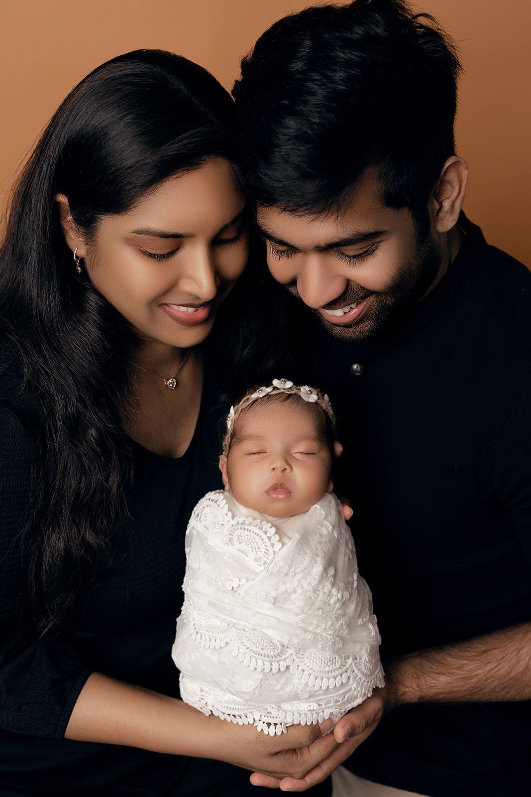 A man and woman are holding a newborn baby wrapped in a white blanket.