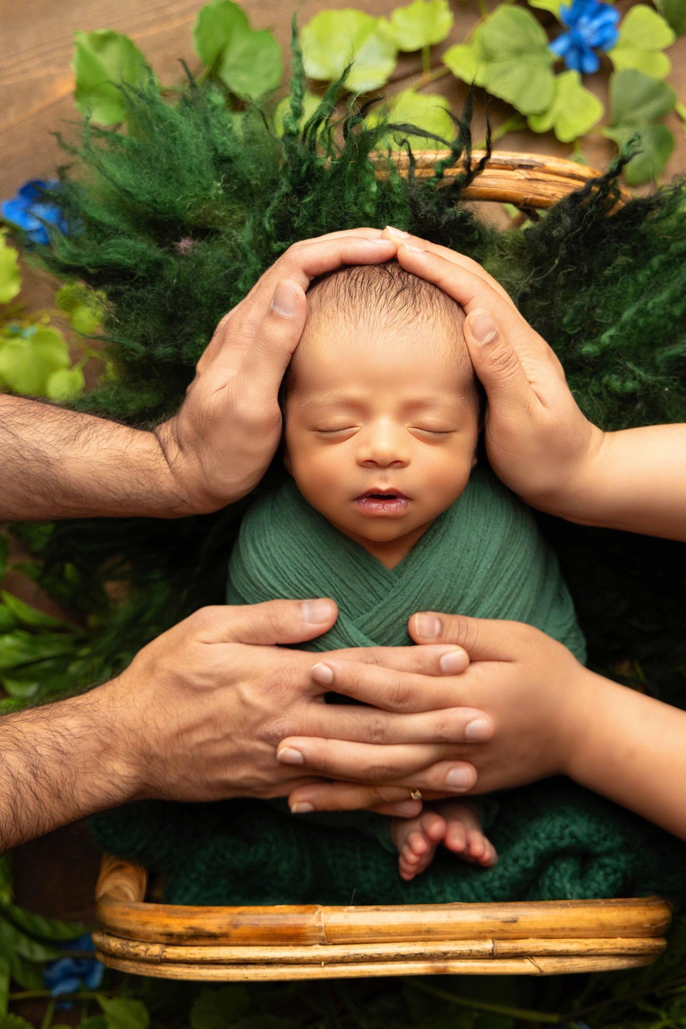 A newborn baby wrapped in a green blanket is being held by two people.