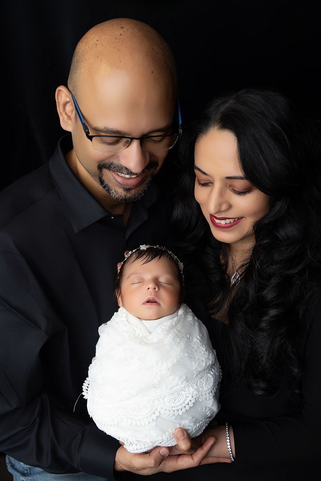 A man and woman are holding a newborn baby wrapped in a white blanket.