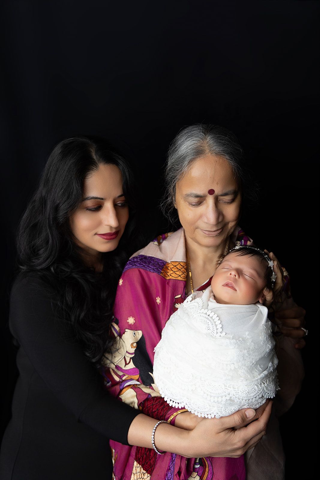 A woman and an older woman are holding a newborn baby.