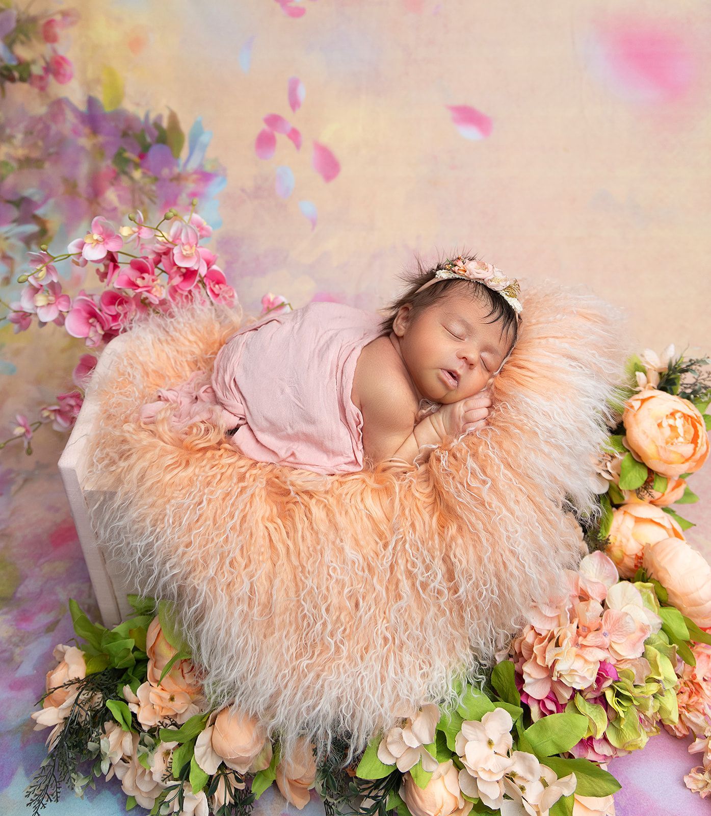A newborn baby is sleeping in a basket surrounded by flowers.