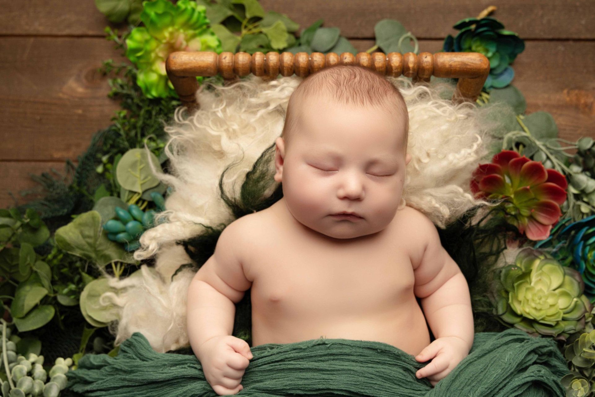 A newborn baby is sleeping in a wooden bed surrounded by flowers.