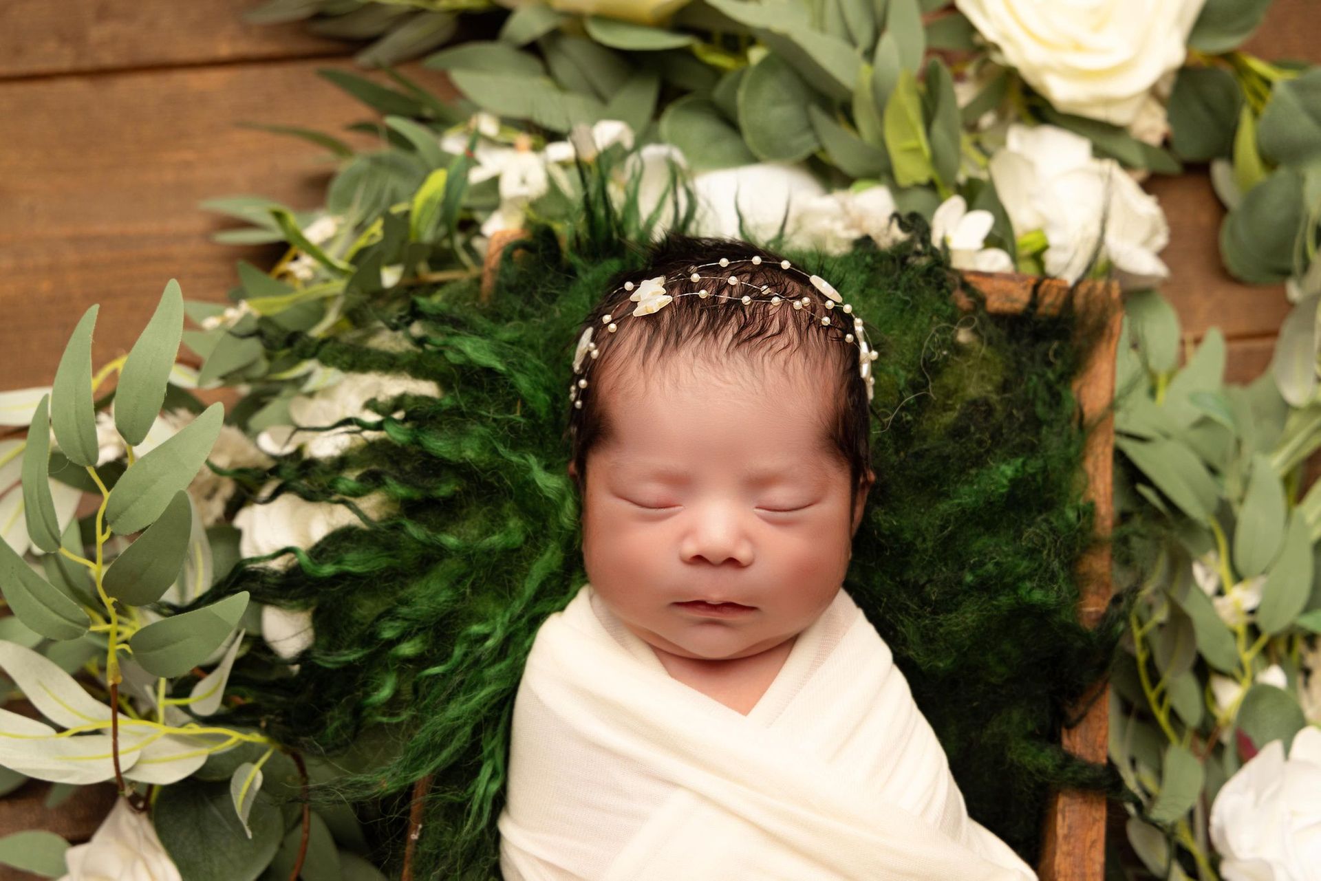 A newborn baby is wrapped in a white blanket and surrounded by flowers.