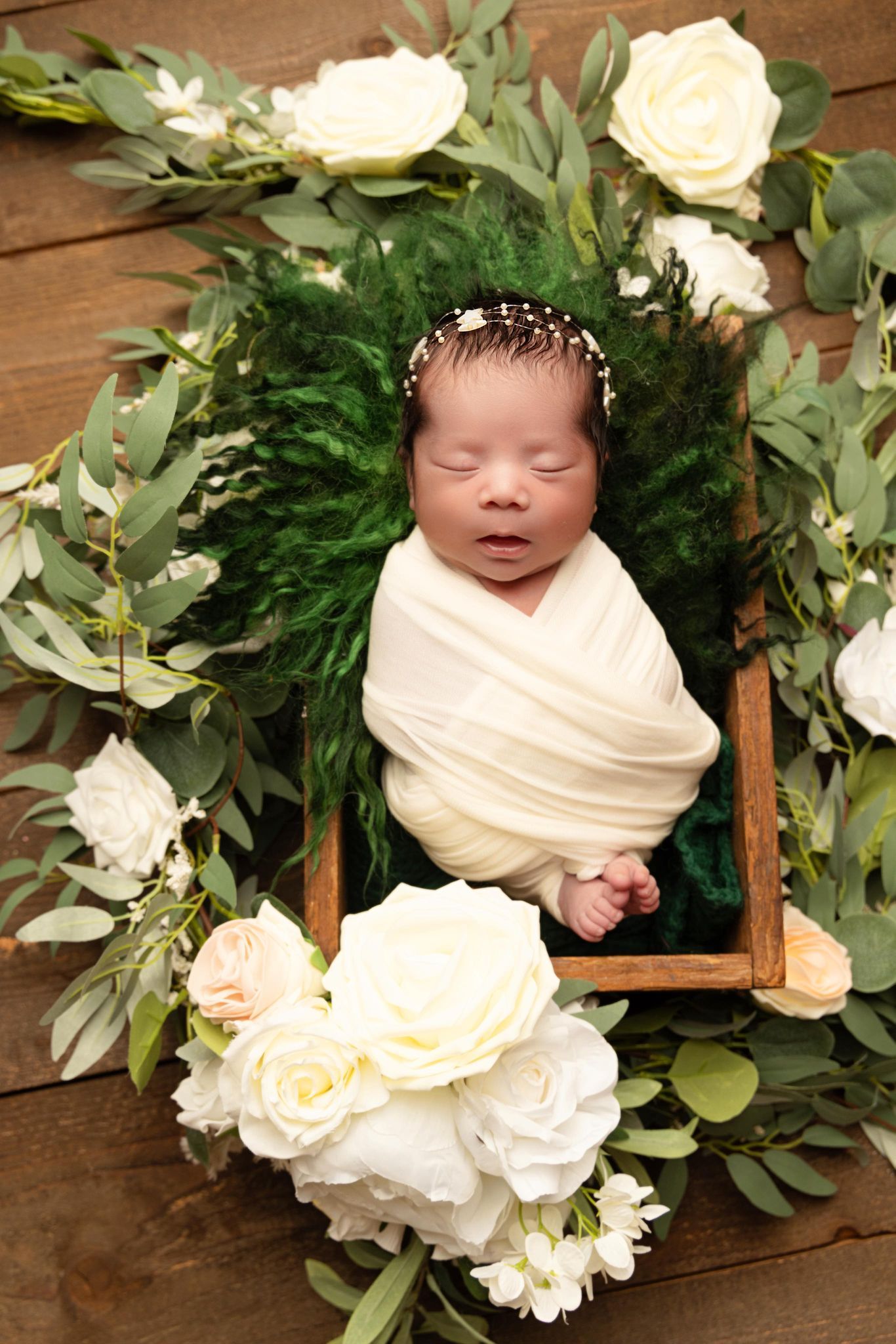 A newborn baby is sleeping in a wooden box surrounded by flowers.