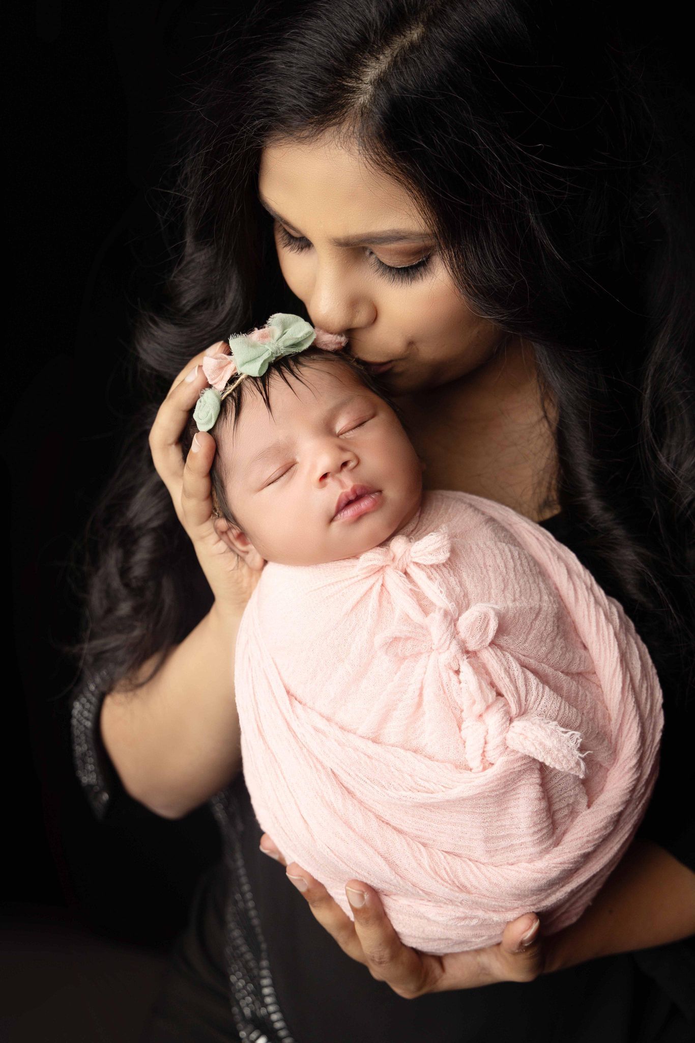 A woman is kissing her newborn baby on the cheek.