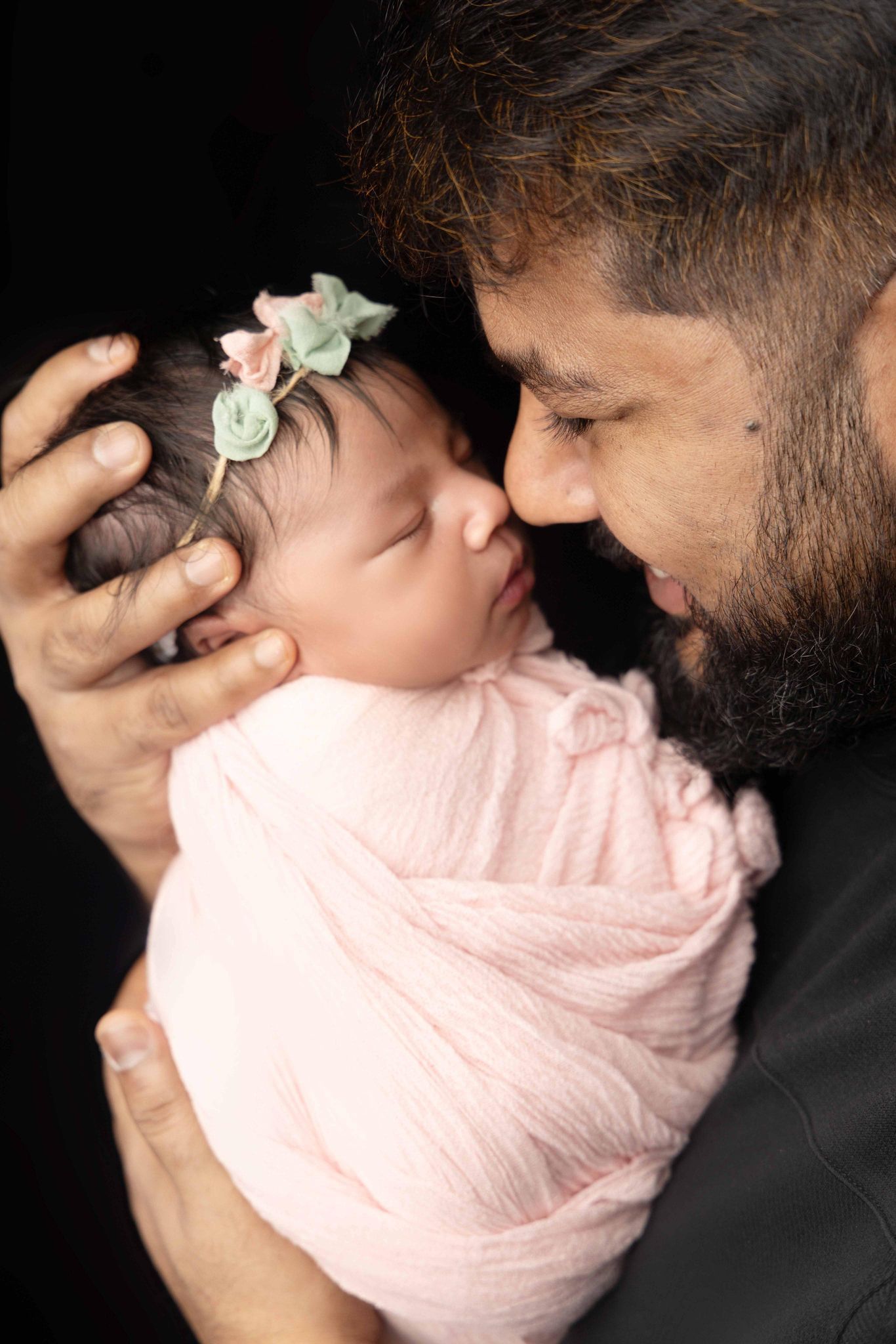 A man is holding a newborn baby wrapped in a pink blanket.