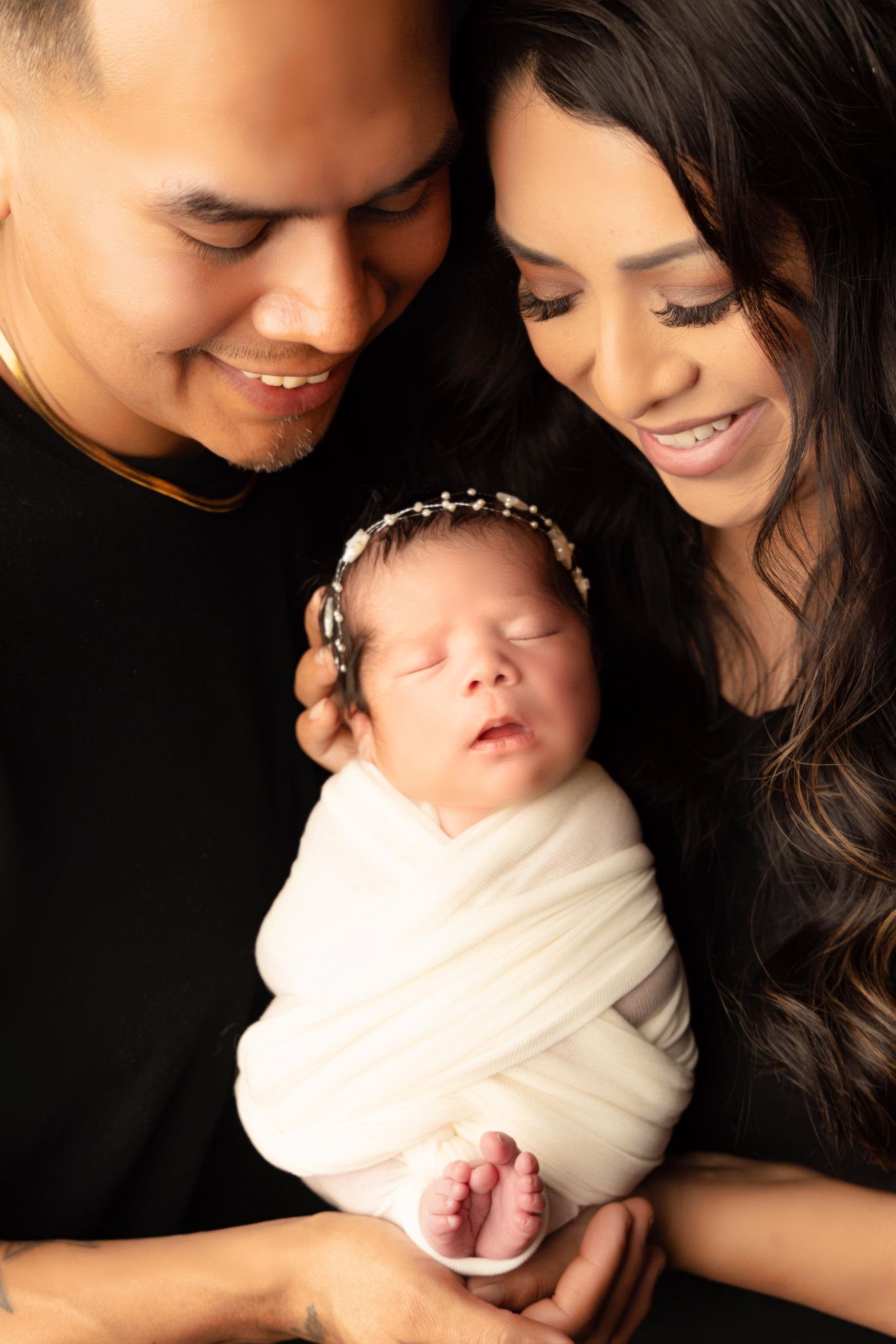 A man and woman are holding a newborn baby wrapped in a white blanket.