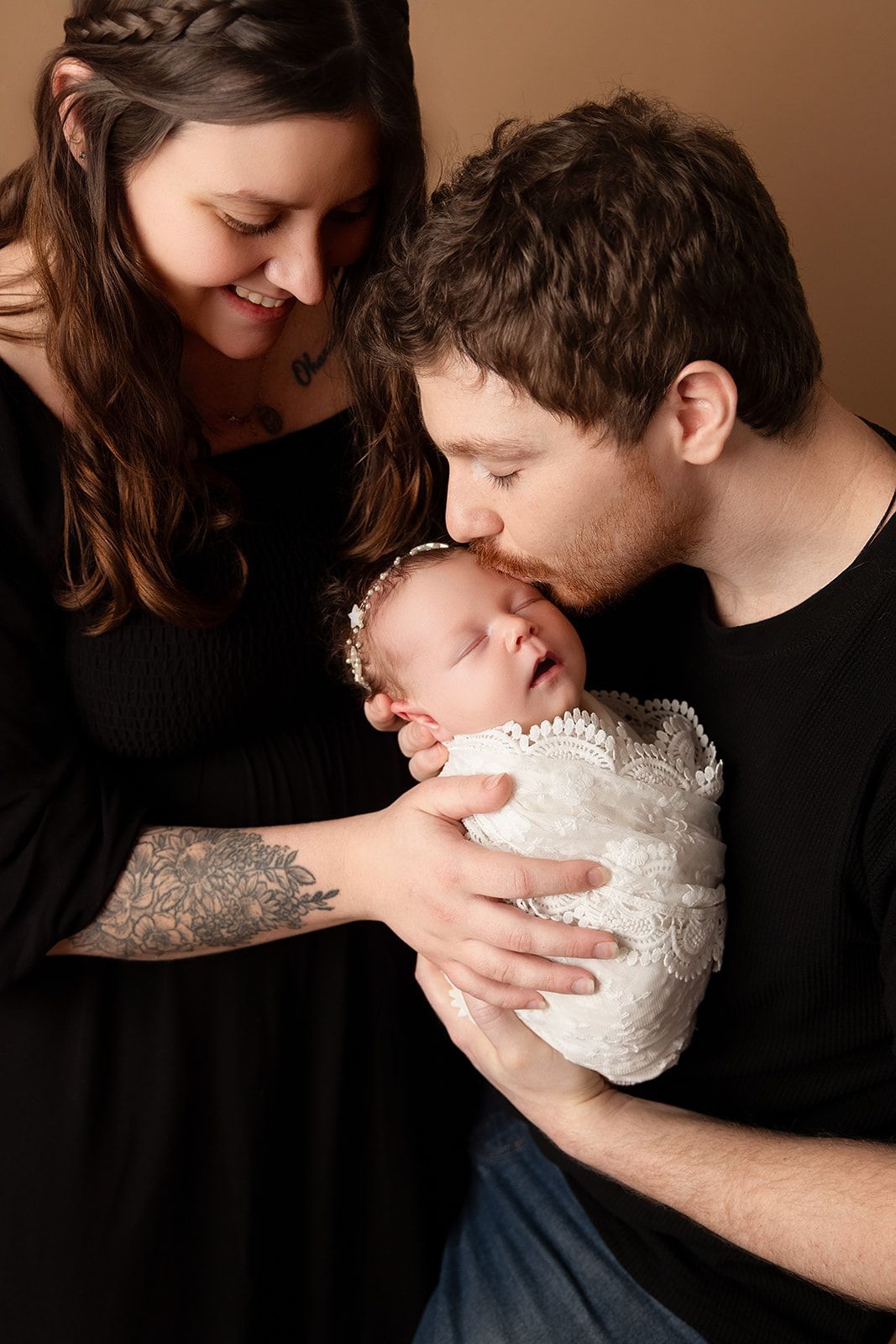 A man is kissing a woman on the cheek while holding a newborn baby.