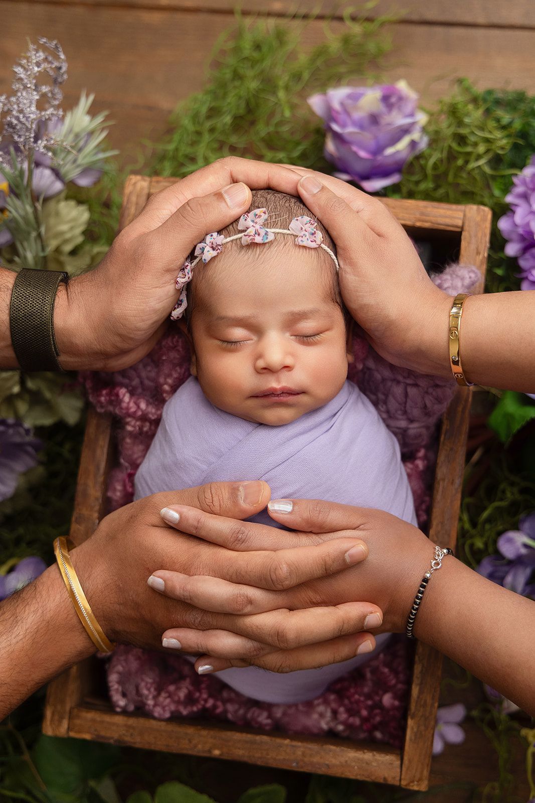 A newborn baby wrapped in purple blanket is being held by two people.