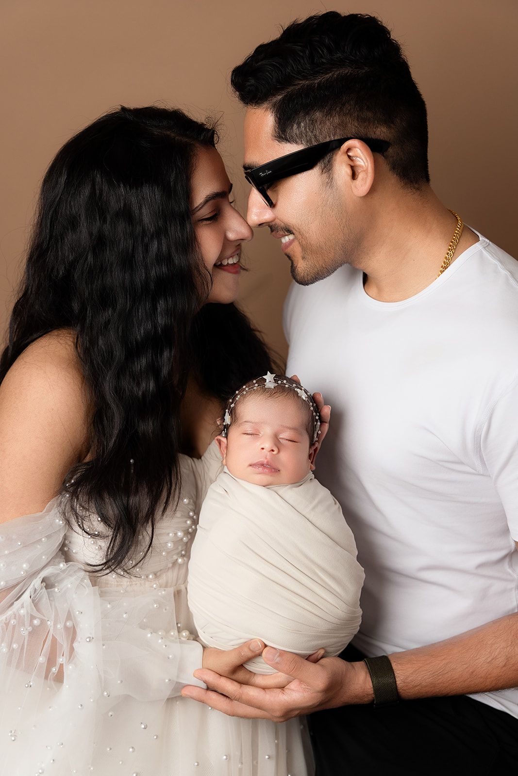 A man and a woman are holding a newborn baby wrapped in a blanket.