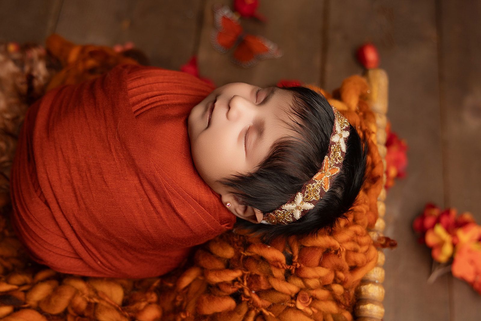 A newborn baby wrapped in an orange blanket is sleeping in a basket.