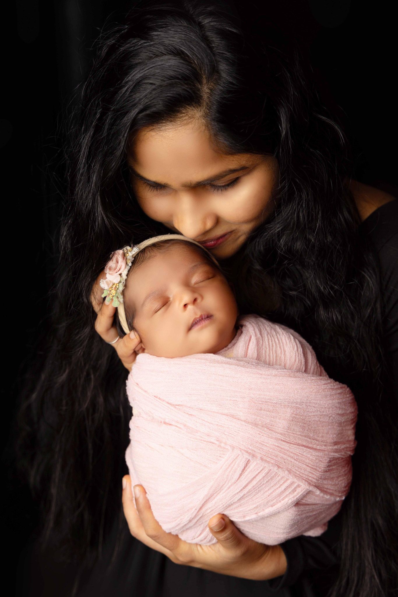 A woman is holding a newborn baby wrapped in a pink blanket.