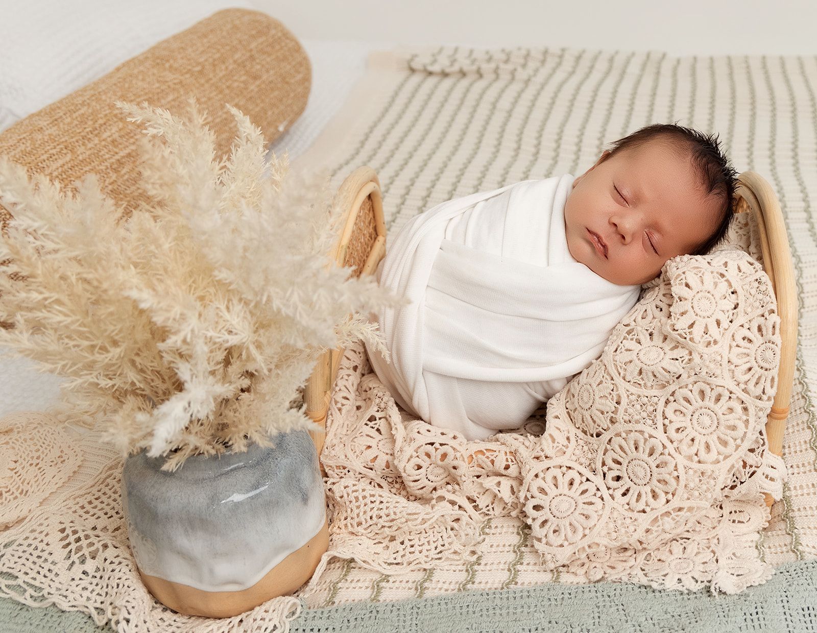 A newborn baby wrapped in a white blanket is sleeping in a basket.