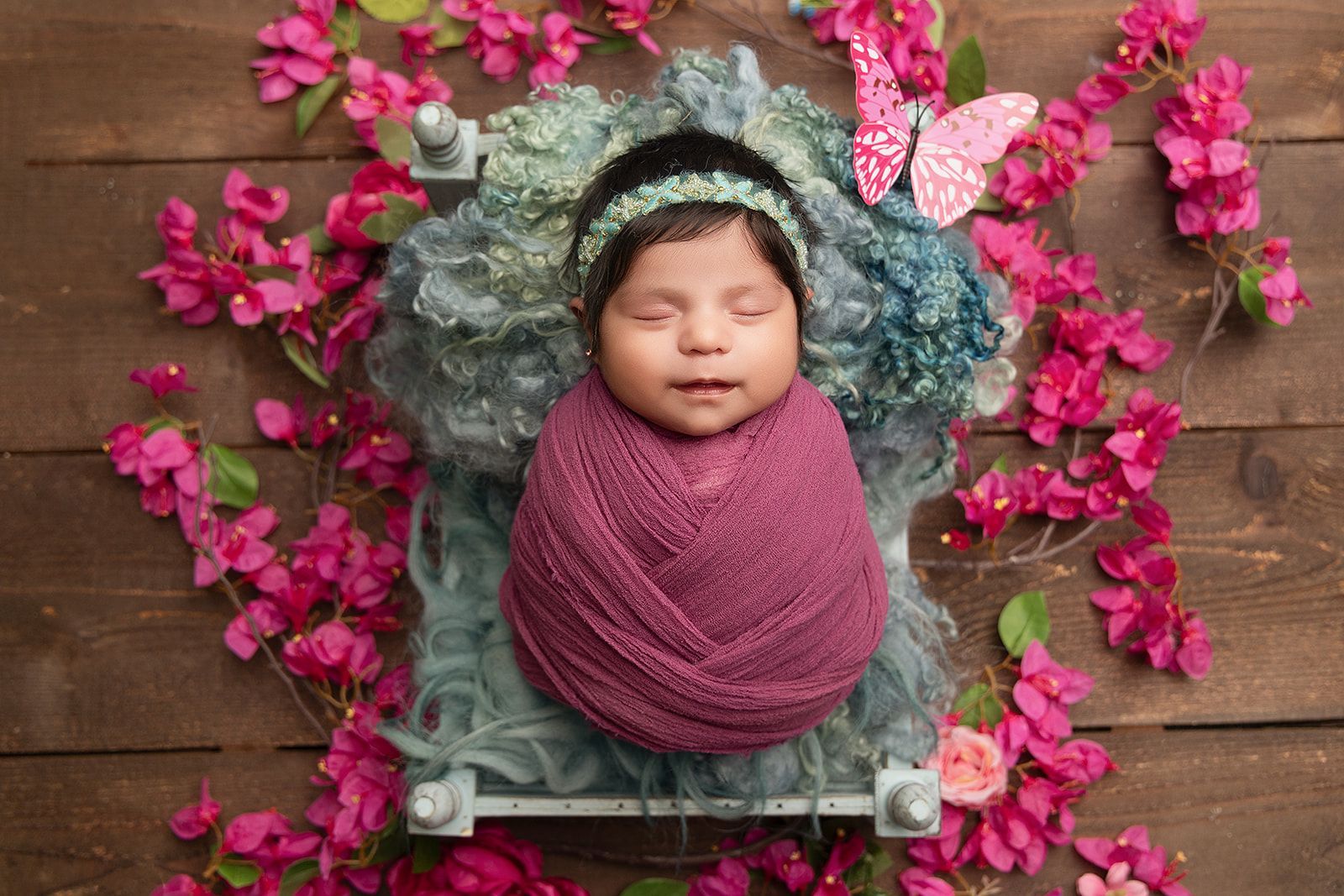 A newborn baby is wrapped in a blanket and surrounded by pink flowers.