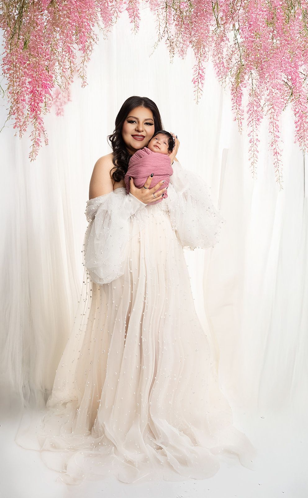 A woman in a white dress is holding a baby in her arms.