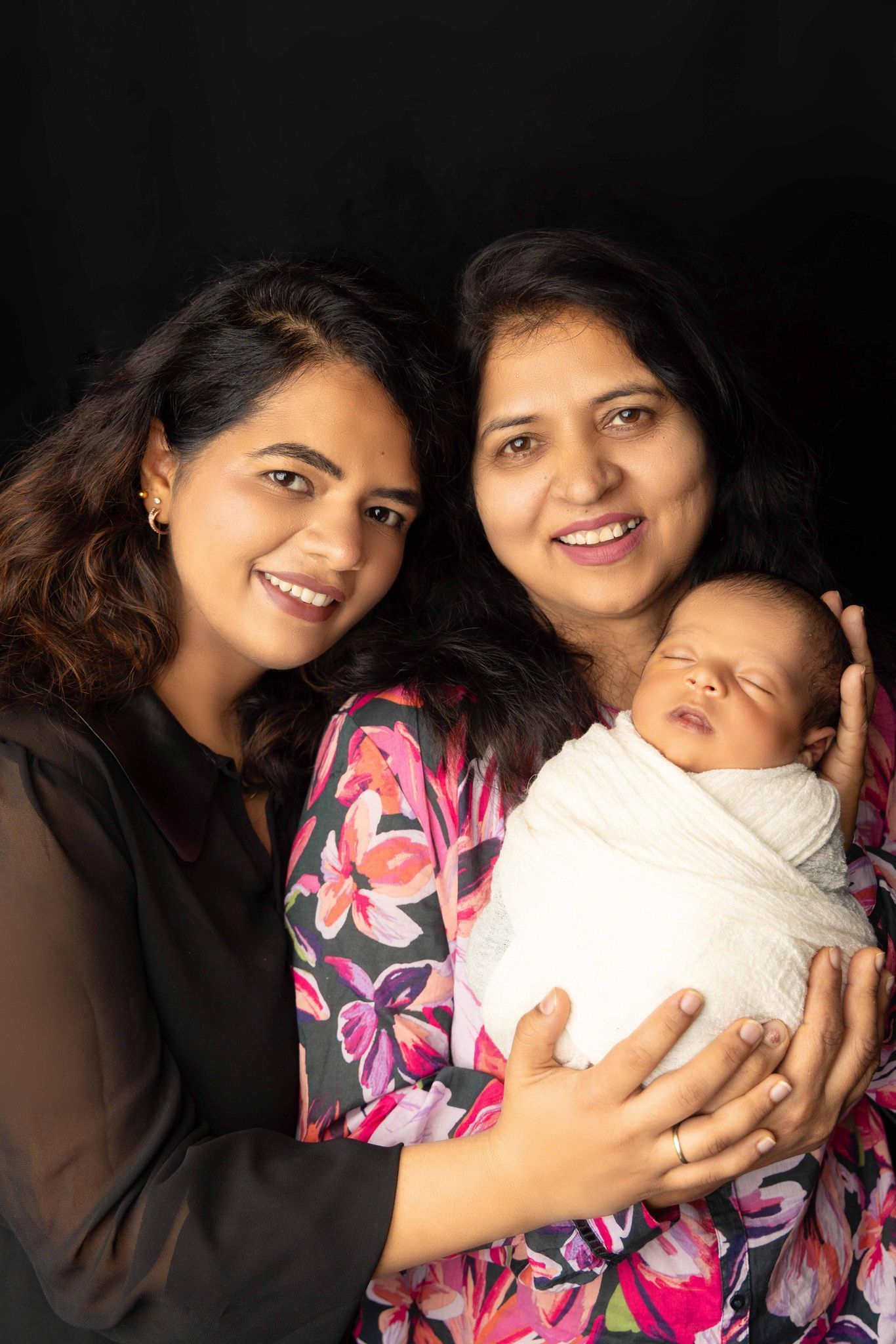 Two women are holding a newborn baby wrapped in a blanket.