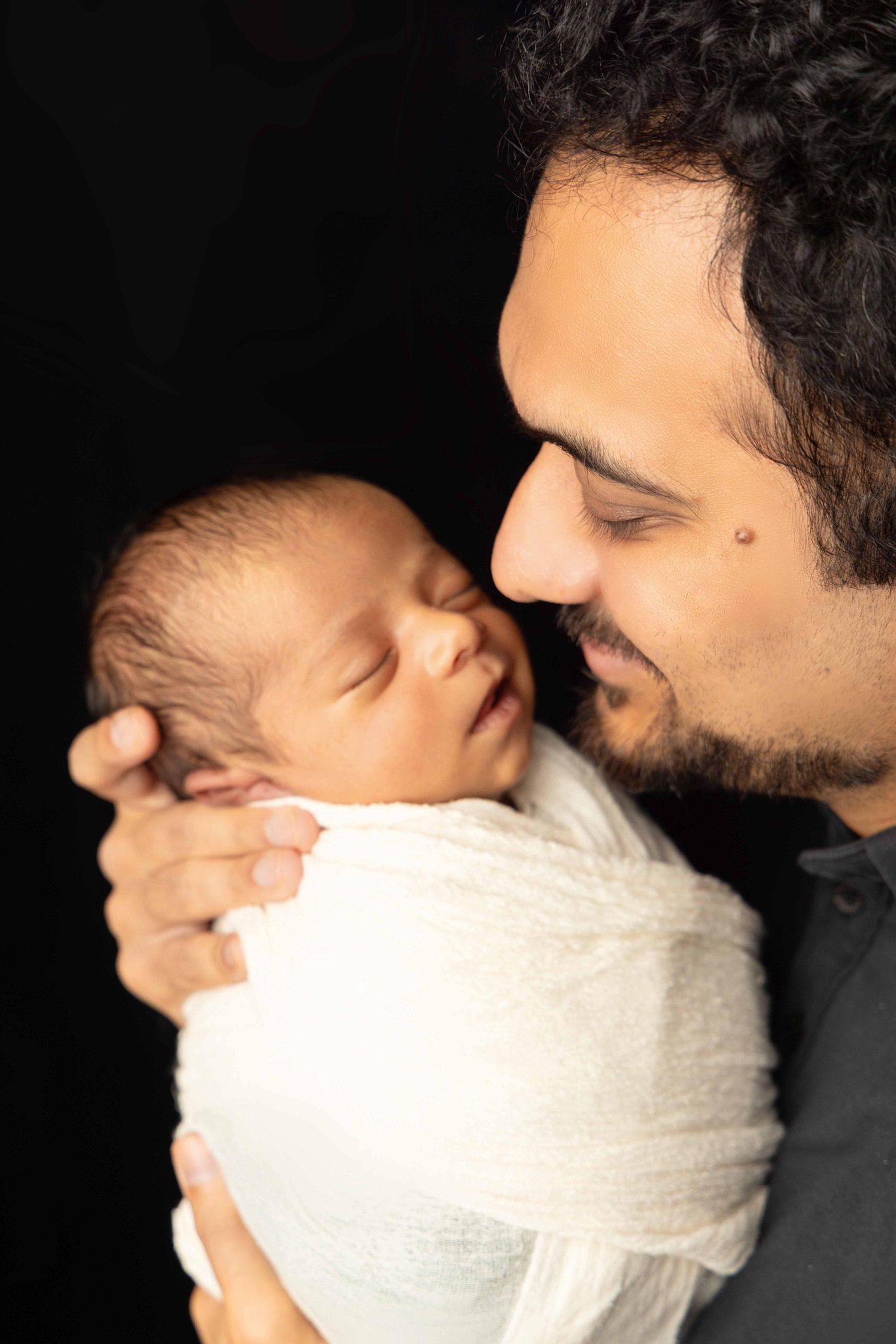 A man is holding a newborn baby wrapped in a white blanket.