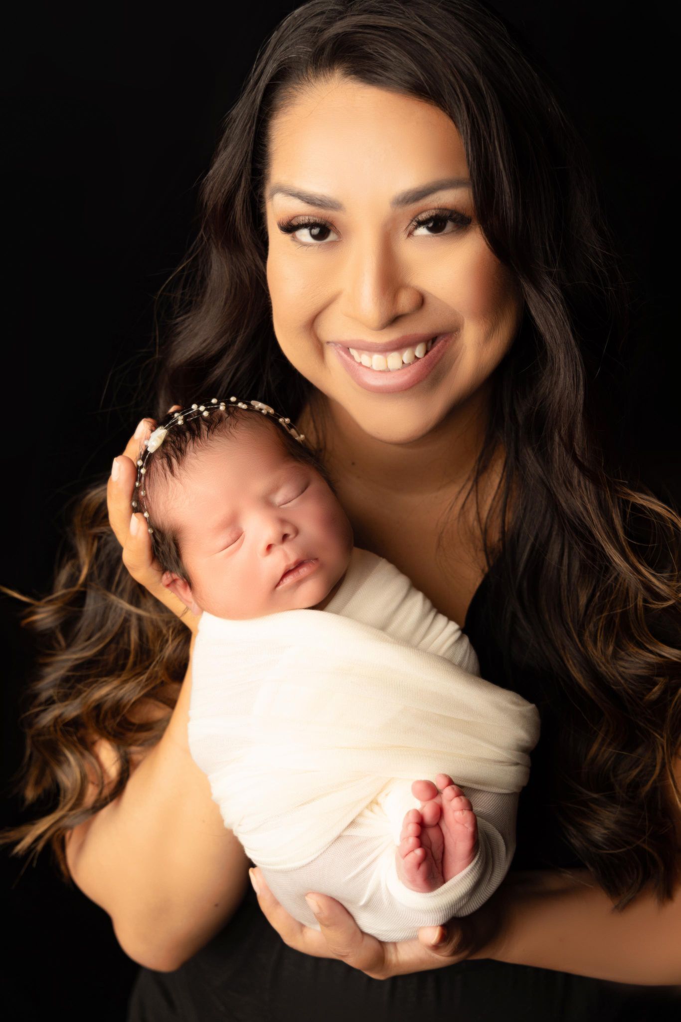 A woman is holding a newborn baby wrapped in a white blanket.
