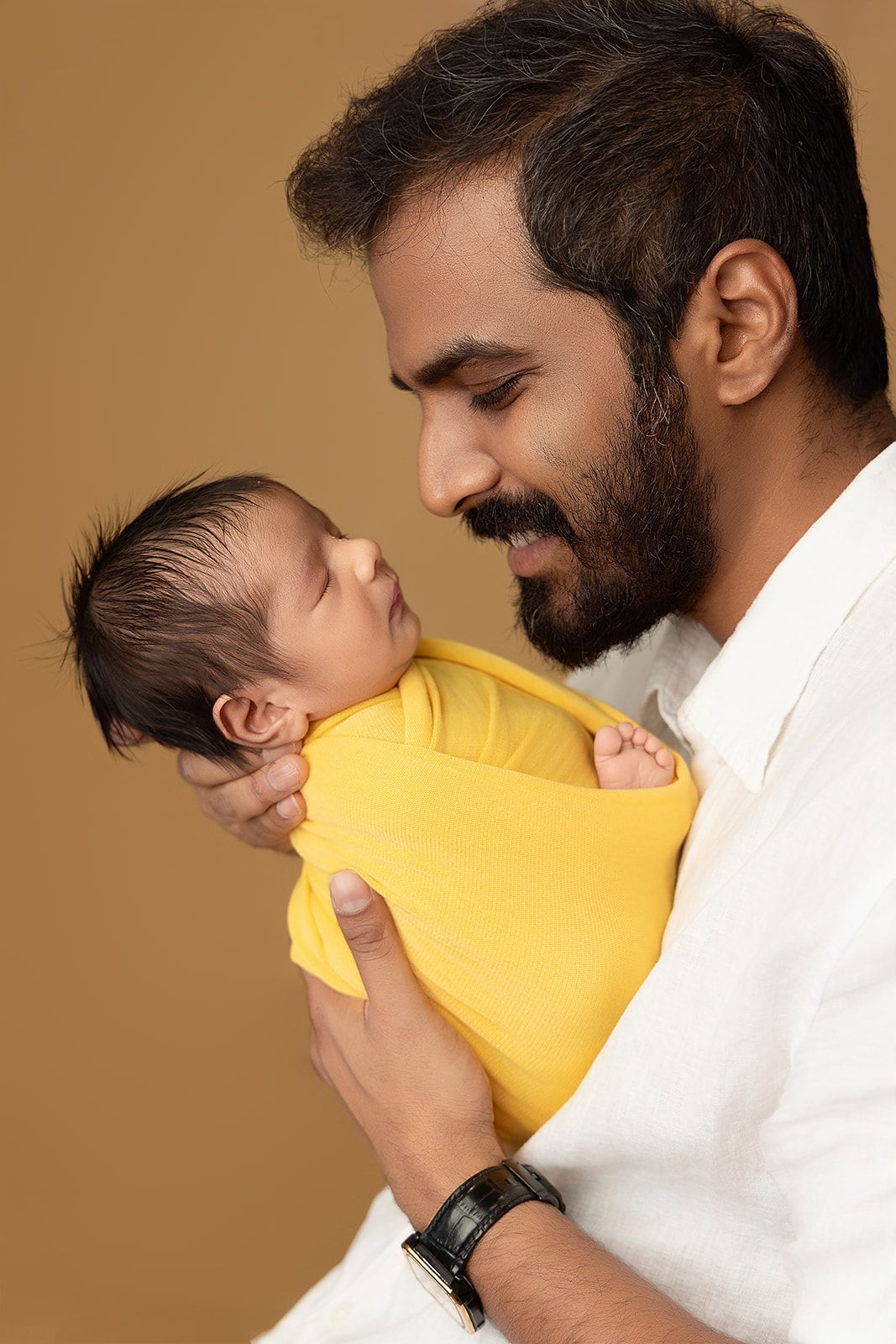 A man is holding a newborn baby wrapped in a yellow blanket.