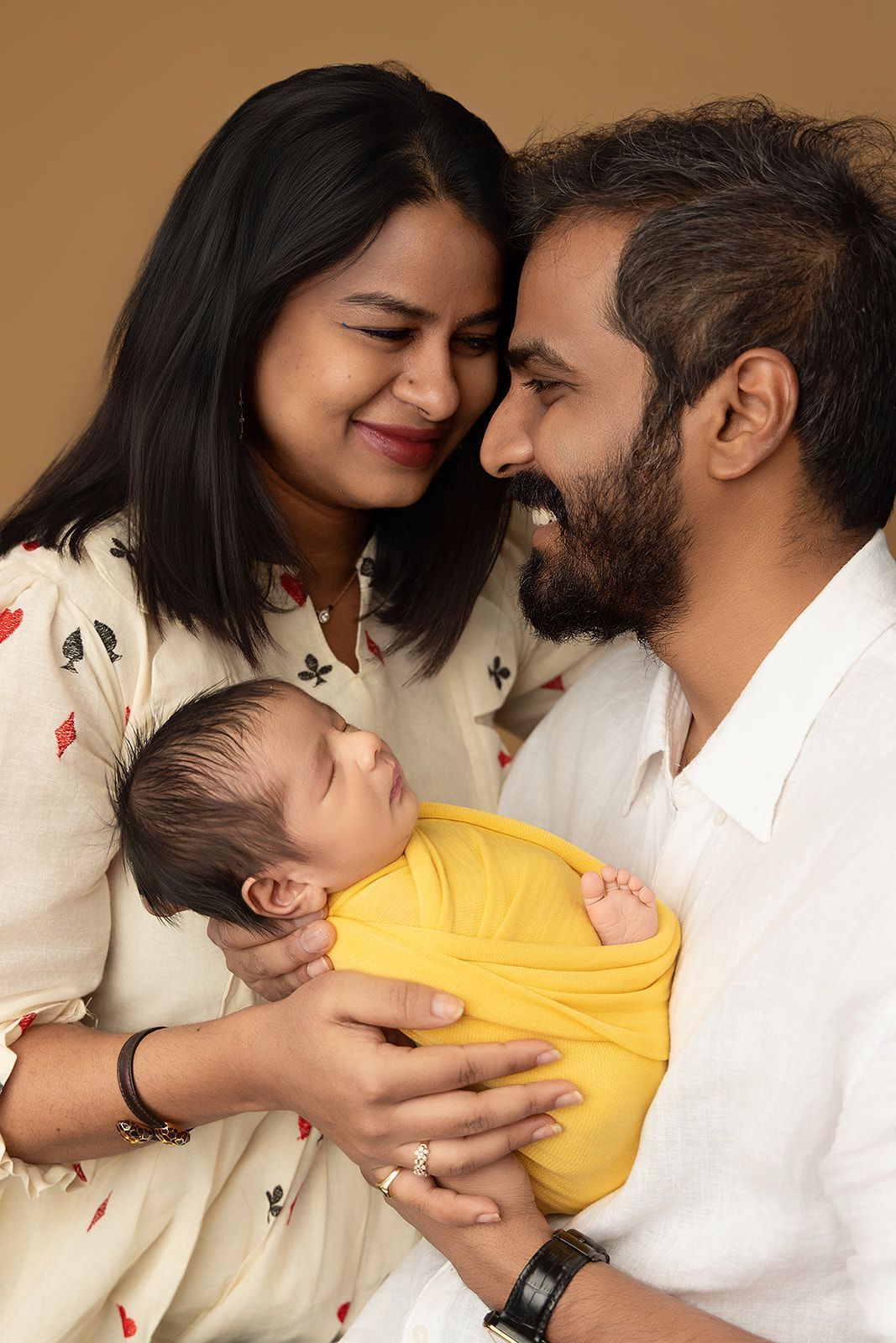 A man and woman are holding a newborn baby wrapped in a yellow blanket.