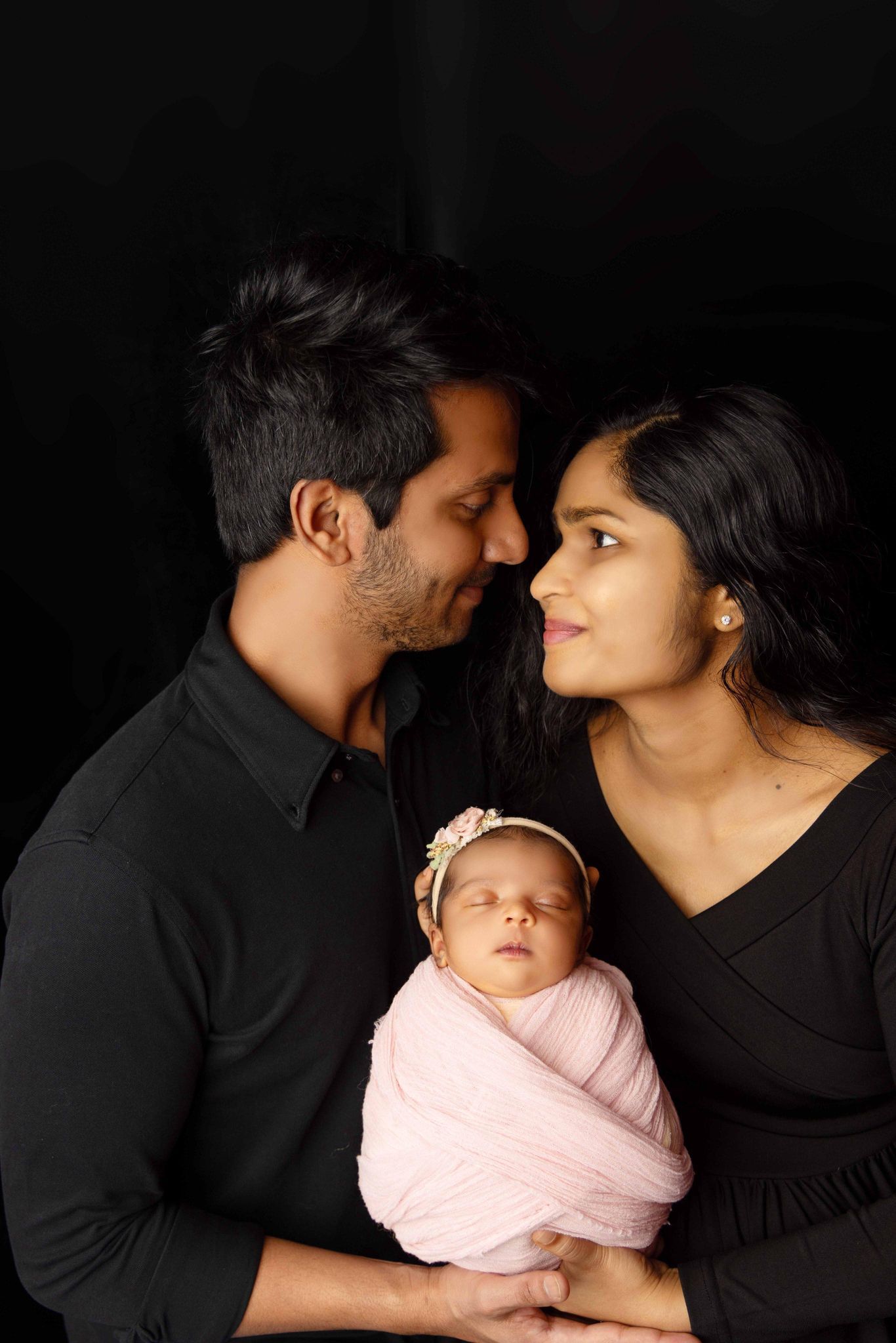 A man and woman are holding a newborn baby wrapped in a pink blanket.