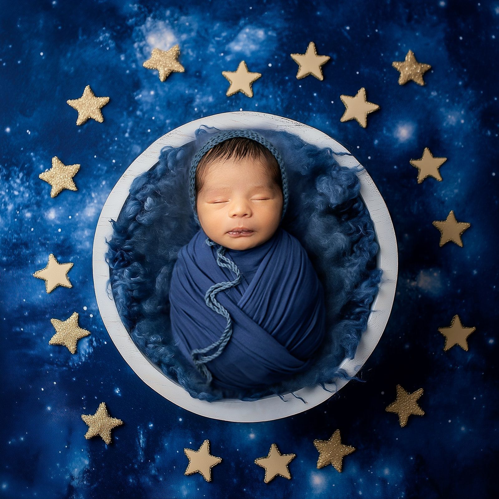 A baby wrapped in a blue blanket is sleeping in a bowl surrounded by stars