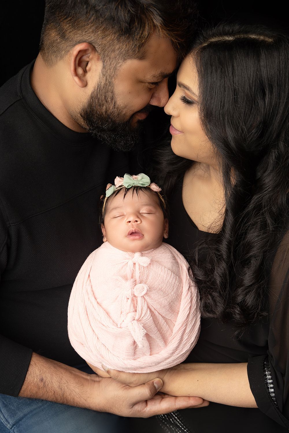 A man and woman are holding a newborn baby wrapped in a pink blanket