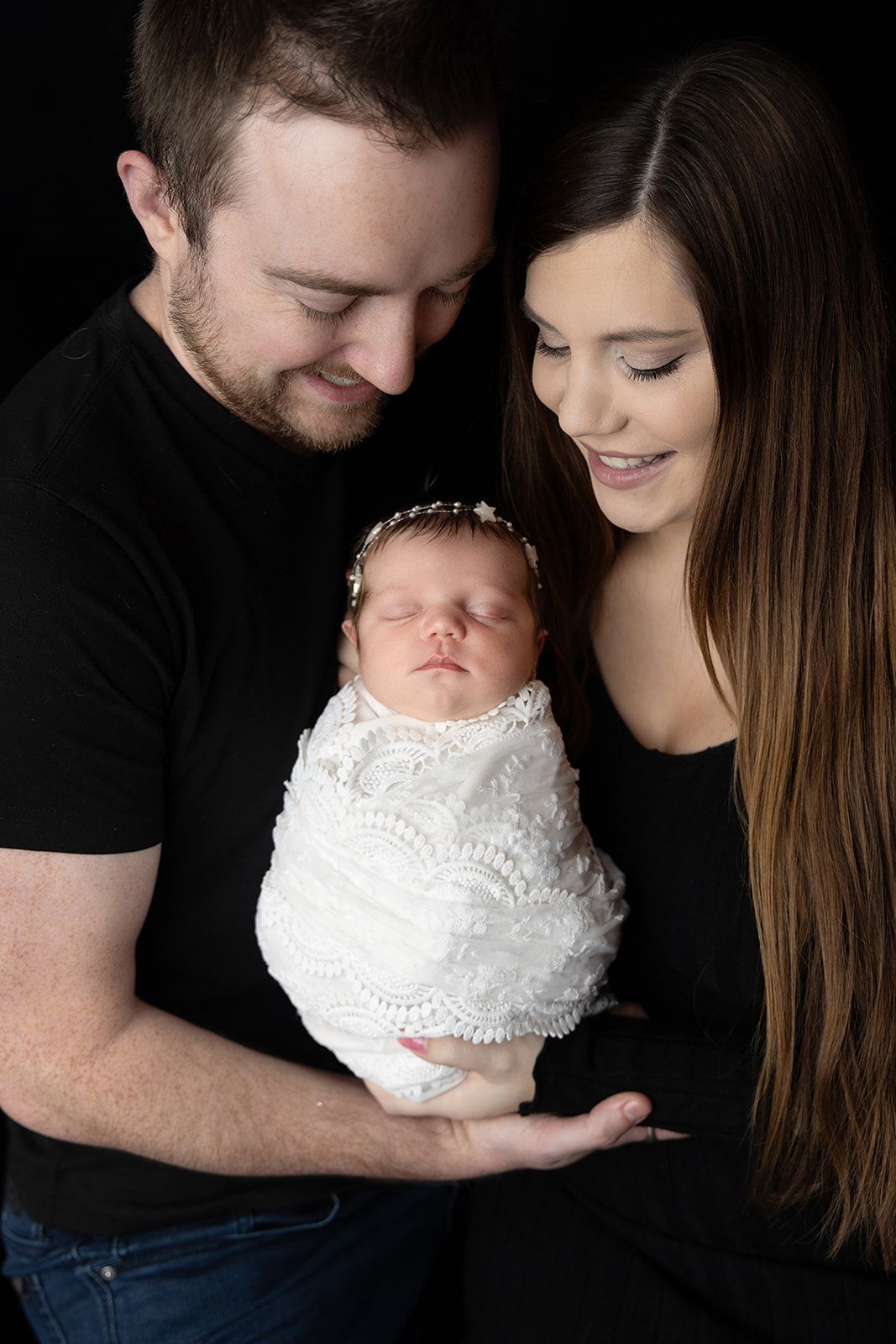 A man and woman are holding a newborn baby wrapped in a white blanket