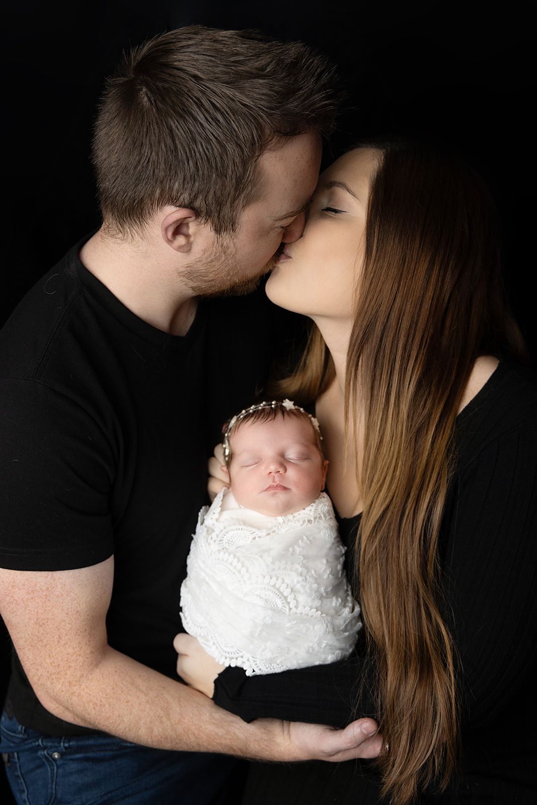 Couple kissing while holding newborn baby
