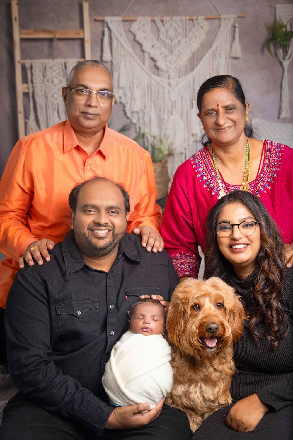 A family is posing for a picture with a newborn baby and a dog
